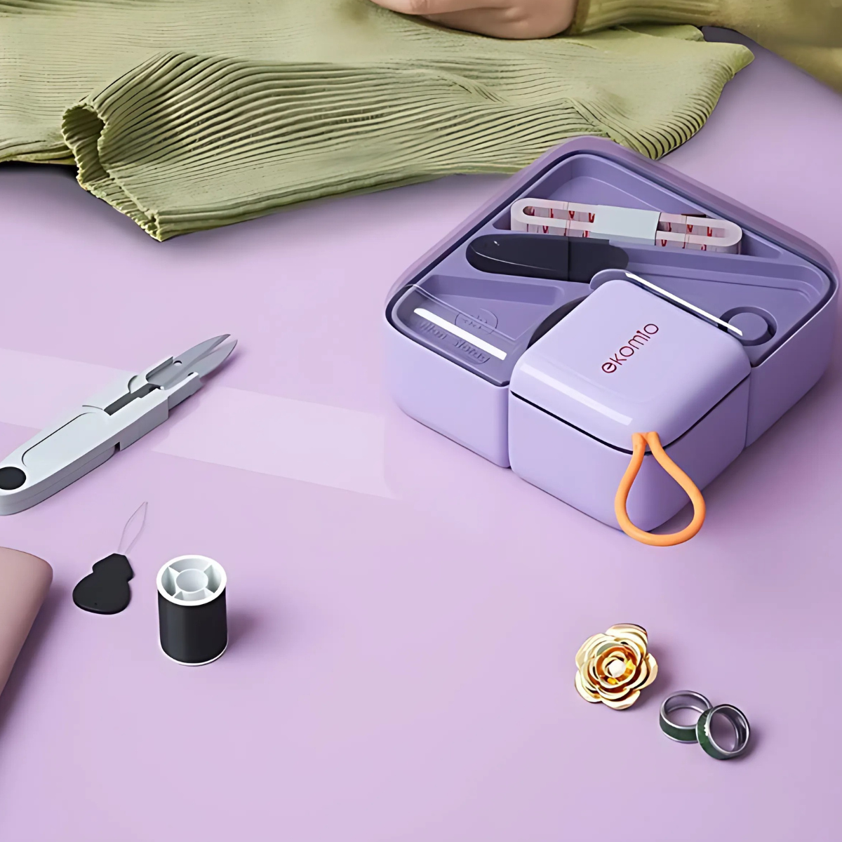 The Mini Sewing Kit, in lavender, includes threads, scissors, needle, thimble, and tape measure. Compact and portable, it's shown on a pink surface with fabric and pins—perfect essentials for a quilting retreat.