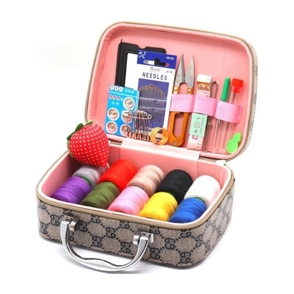The Sewing Kit In a Stylish Box includes multiple colored thread spools, needles, scissors, a strawberry pin cushion, buttons, and assorted sewing tools neatly organized in a patterned case.