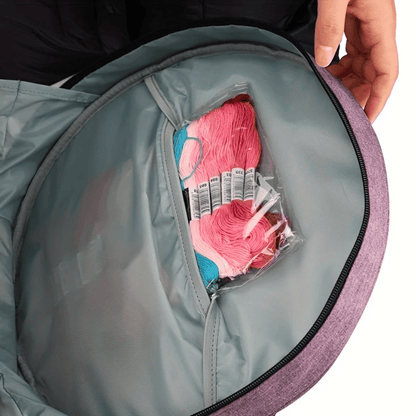A hand gently holds the top of the open Embroidery Storage Bag, unveiling a transparent pocket filled with pink and blue embroidery thread skeins, essential for sewing.