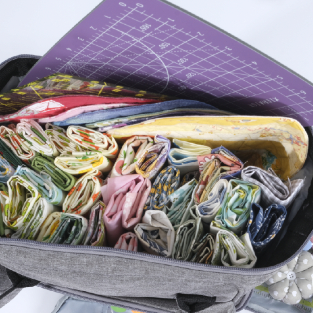 The Premium Quilting Organizer Backpack, made from durable 600D Oxford fabric in gray, holds colorful rolled fabrics, essential sewing and quilting tools, and is topped with a purple cutting mat.