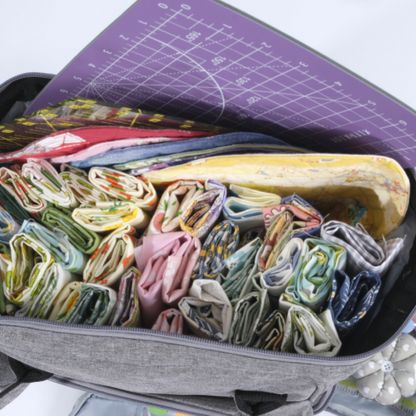 The Premium Quilting Organizer Backpack, made from durable 600D Oxford fabric in gray, holds colorful rolled fabrics, essential sewing and quilting tools, and is topped with a purple cutting mat.