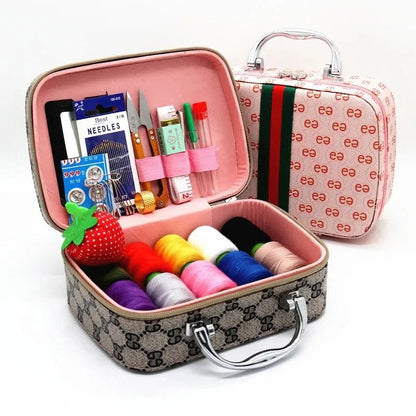 The Sewing Kit In a Stylish Box opens to reveal colorful threads, sewing needles, scissors, and a measuring tape. A charming strawberry pin cushion complements the pink box with its green-red striped lid—ideal for all your sewing projects.